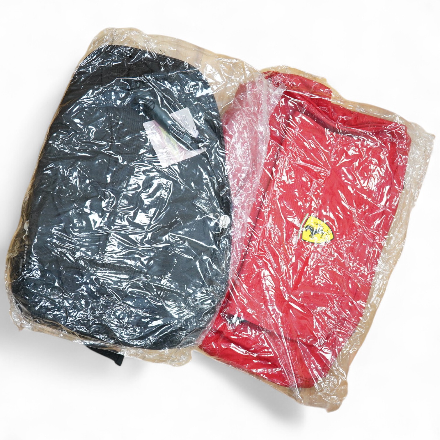 Two official Ferrari branded bags; a backpack and a duffle bag, both new with tags, both contained within an original Ferrari plastic bag dated 2002. Condition - good.